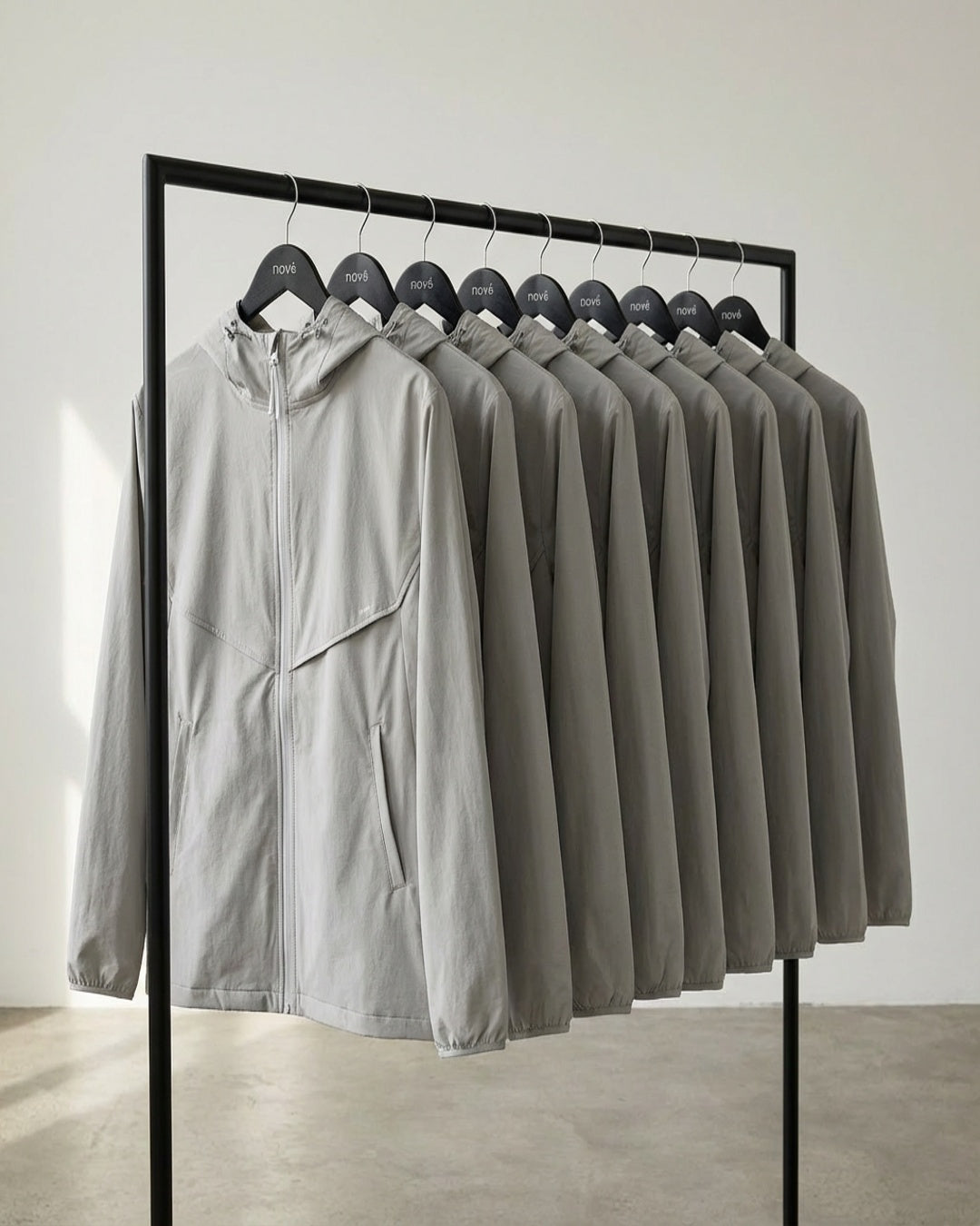 Row of gray jackets on a black rack against a white wall