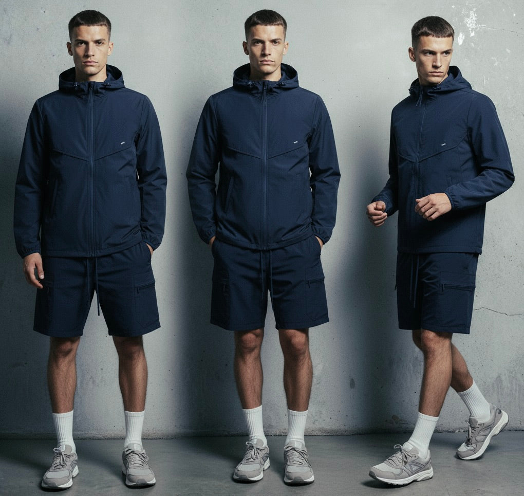 Three men wearing matching navy blue windbreaker and shorts against a gray background