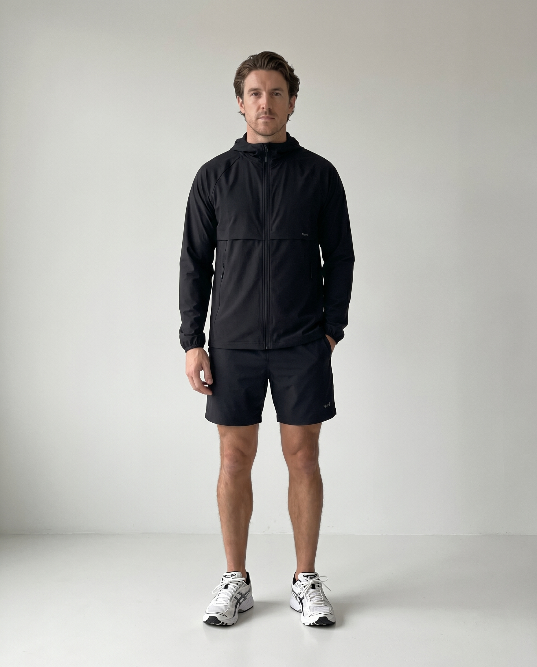 Man wearing a black jacket and shorts standing against a plain background