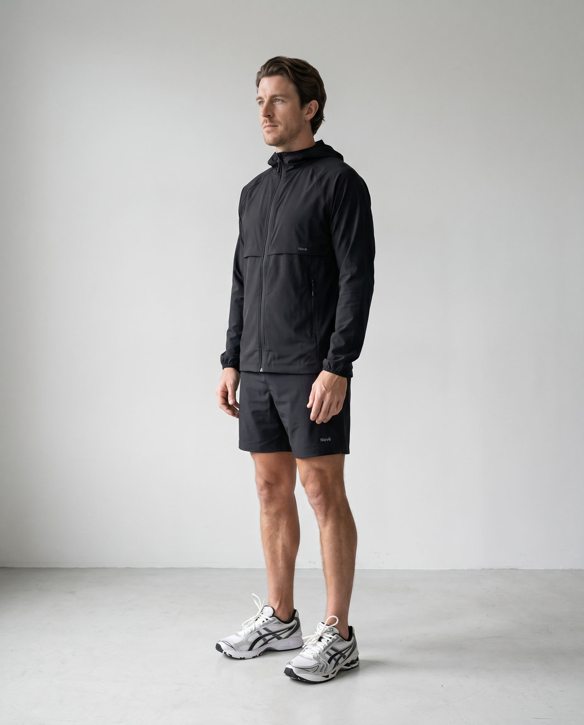 Man wearing a black jacket and shorts standing against a plain background