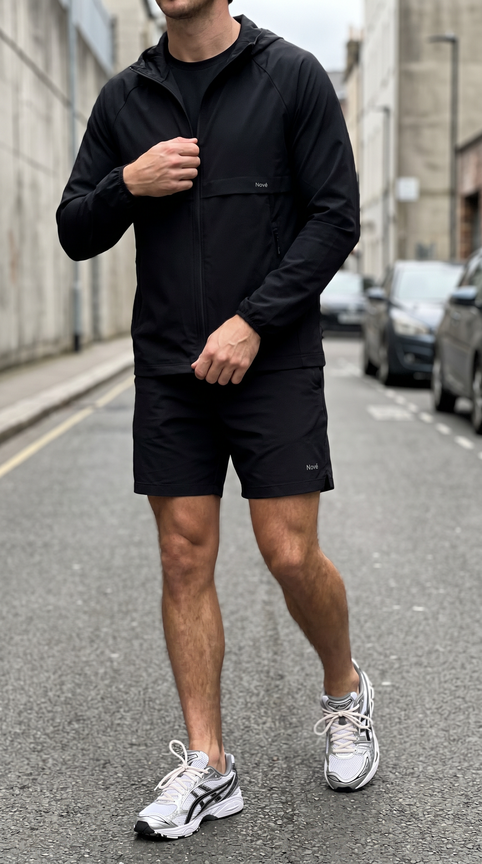 Person wearing a black outfit with white sneakers on a street.