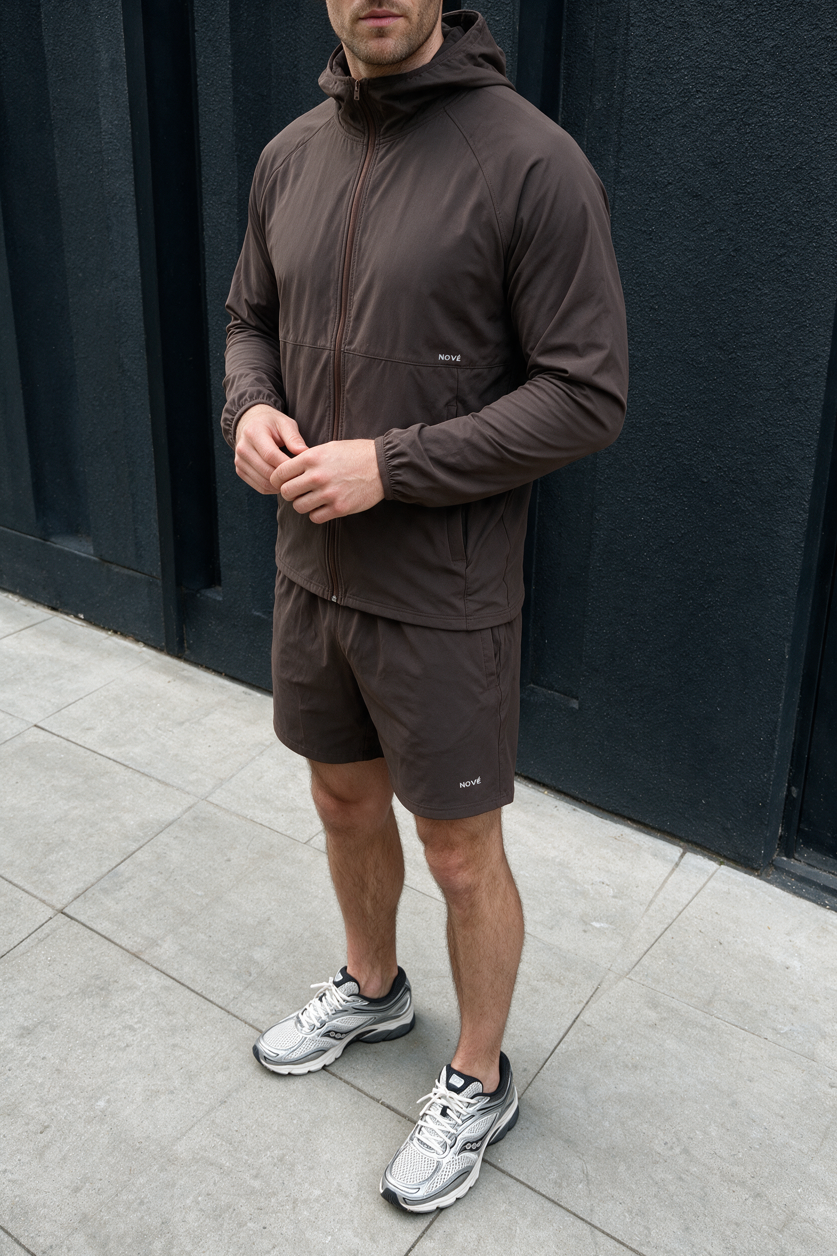 Man wearing the espresso Motion jacket and shorts against a dark wall