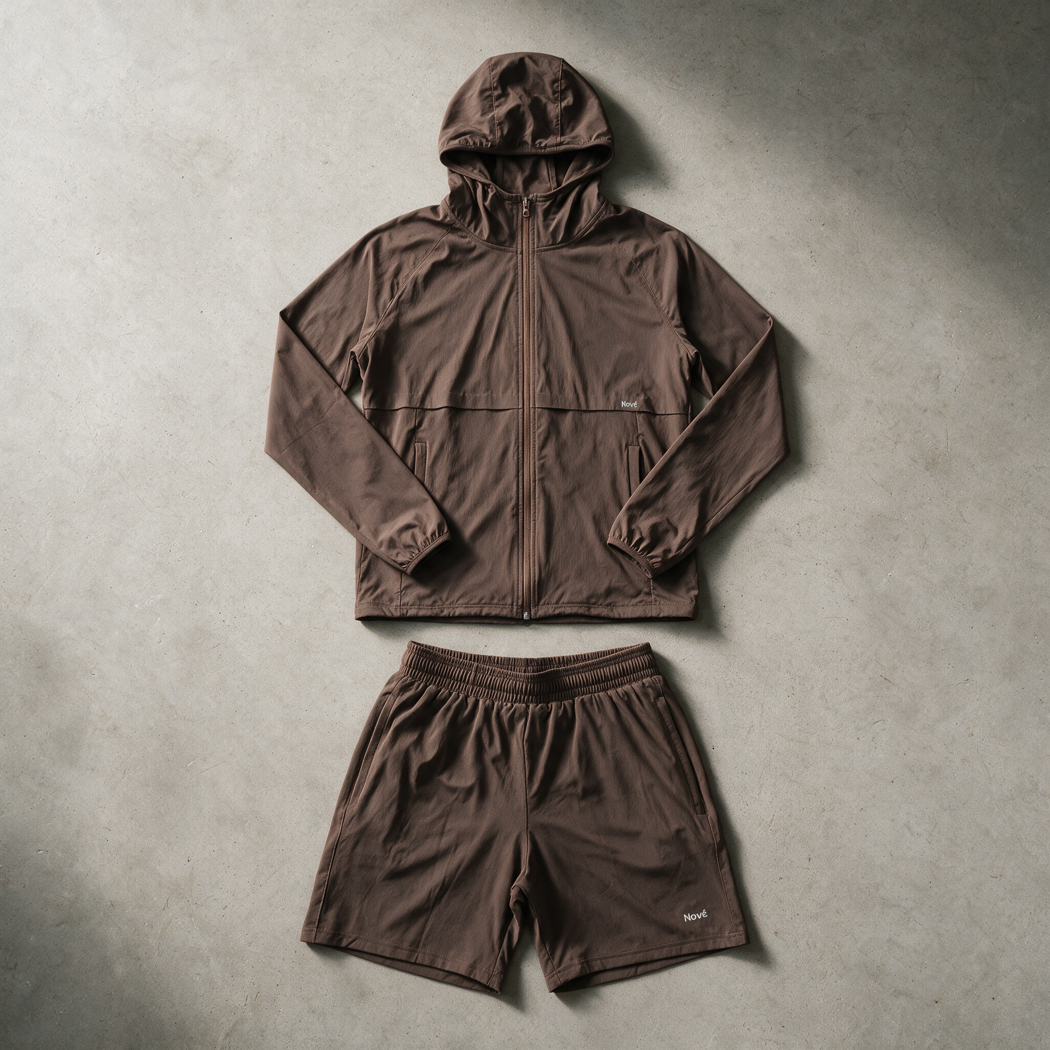 A matching two-piece outdoor set consisting of a brown hooded zip-up jacket and matching shorts, laid flat on a textured gray concrete surface.