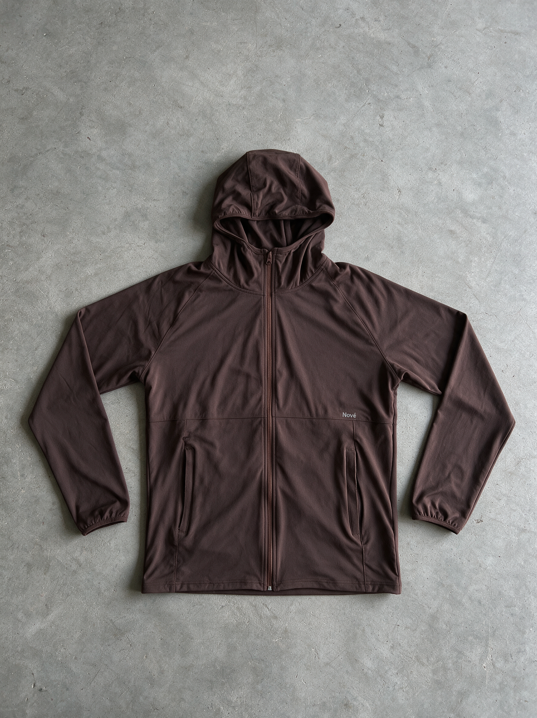 A dark brown hooded zip-up jacket laid flat on a textured gray concrete surface.
