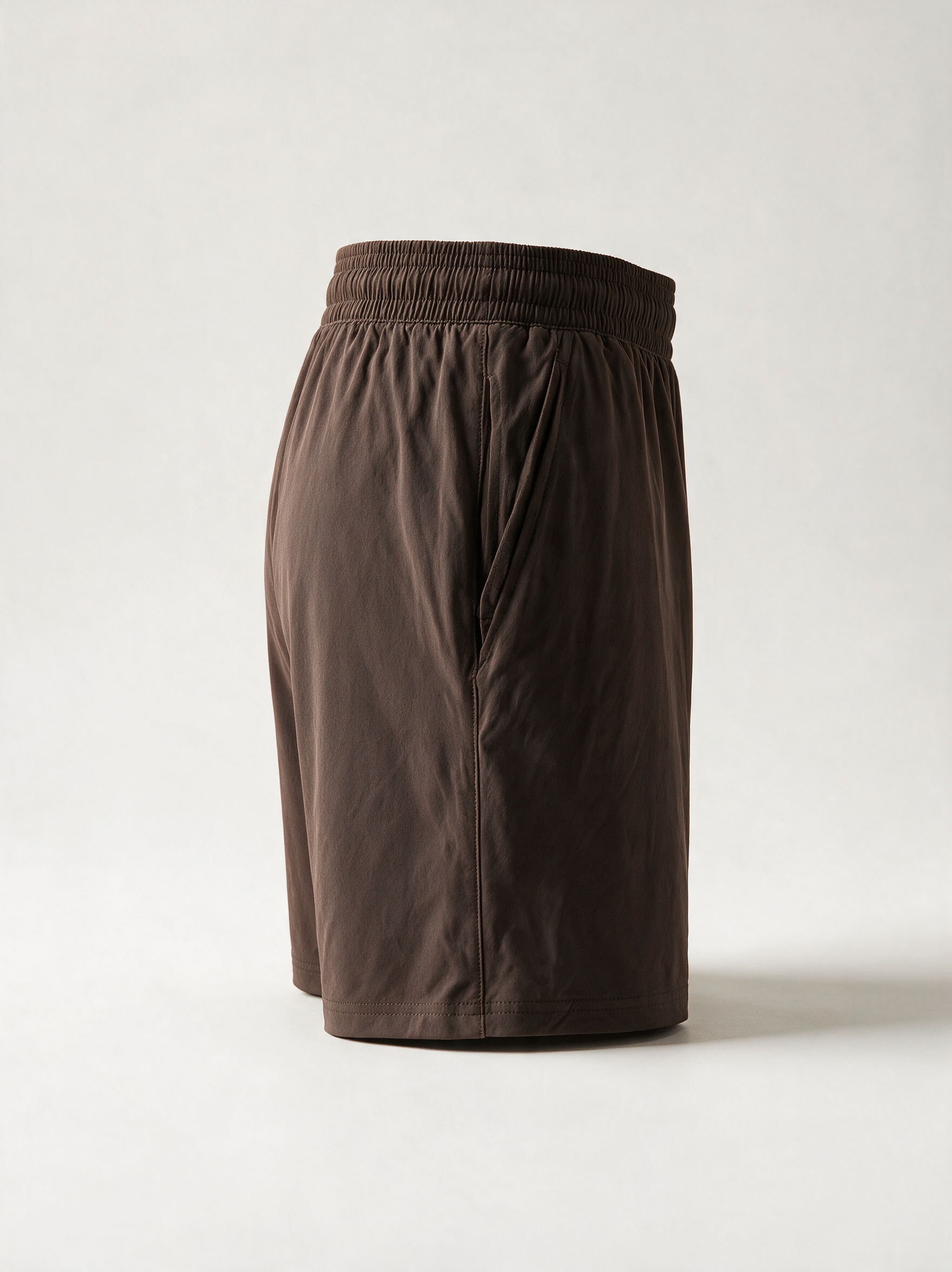A pair of dark brown athletic shorts with an elastic waistband, shown from a three-quarters back view on a light gray studio background.